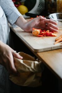 Crop anonymous housewife throwing vegetable leftovers on chopping board while cooking in light kitchen